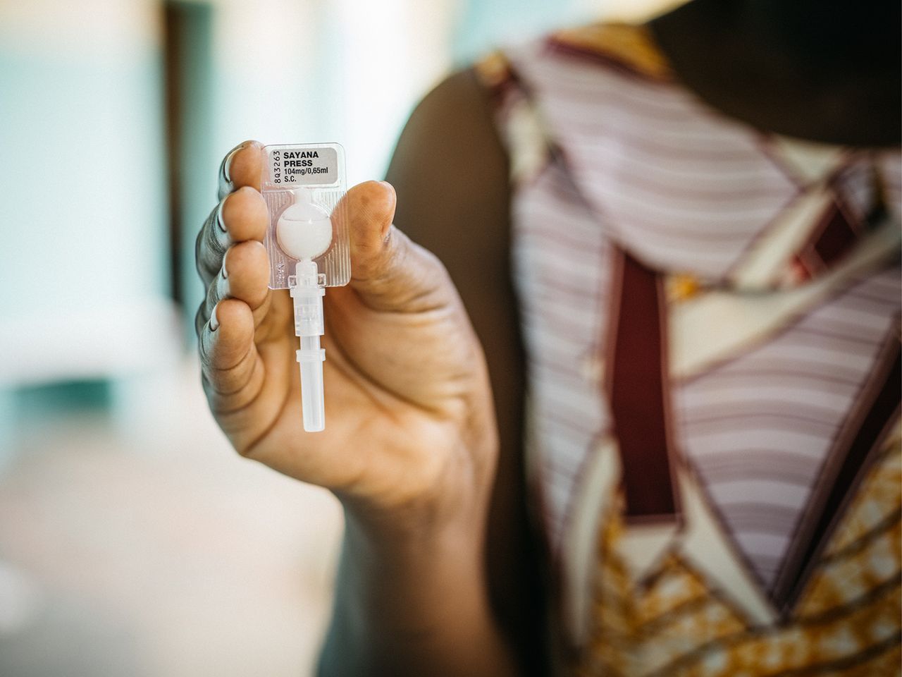A hand holds the Sayana Press injectable.