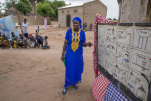 A woman going through the TOSTAN Community Empowerment Program. She stands in front of a chart that teaches women participants about their right to health and their right to be free from all forms of violence, about hygiene, and how diseases are spread and prevented. 